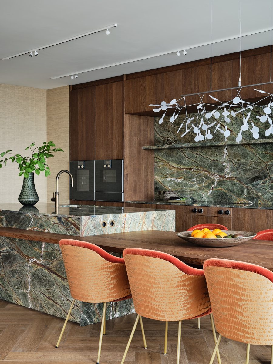 keuken met groen natuursteen, donker notenhout en fluwelen oranje stoelen met een subtiele print.