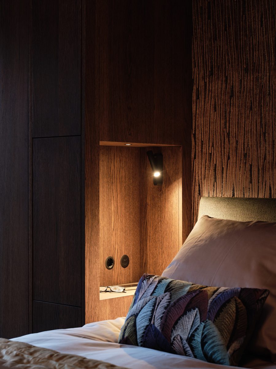 detail foto van nis in maatwerk kast van donker notenhout naast het bed met leuke sierkussens met een vogel veren print