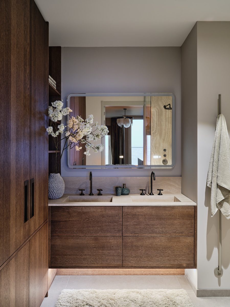 maatwerk wastafel in badkamer met licht natuursteen, donker noten hout en bronzen sanitair