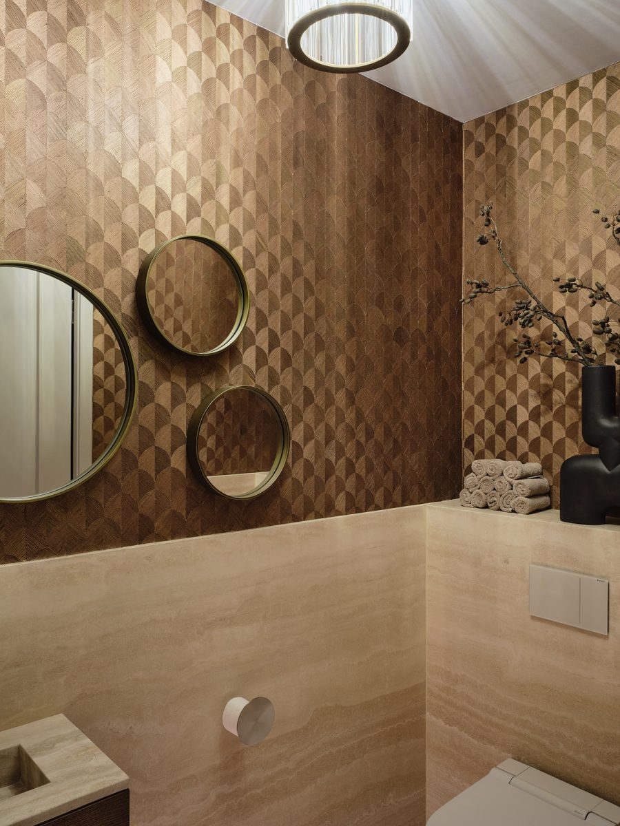 toilet waar gebruik is gemaakt van licht natuursteen, goud behang in schelpvormig patroon en drie spiegels