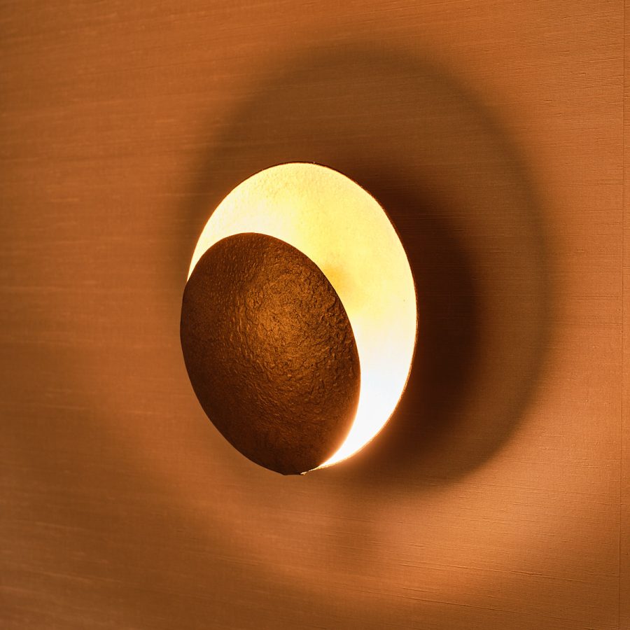 detail foto van een goudkleurige wandlamp dat licht schijnt tegen de muur