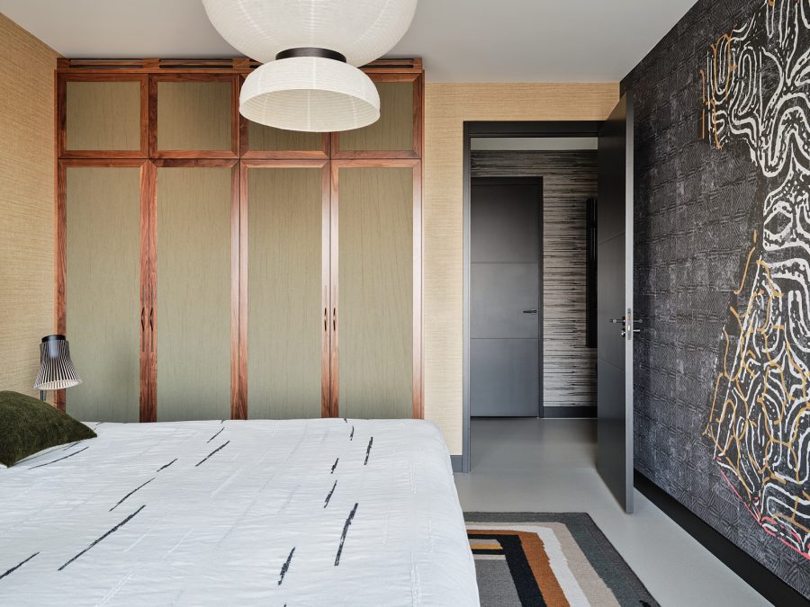 Japandi slaapkamer met houten kastenwand met de deuren ingelegd groen behang. Kusntachtig grijs behang op de wand en oranje en grijs vloerkleed in patroon.