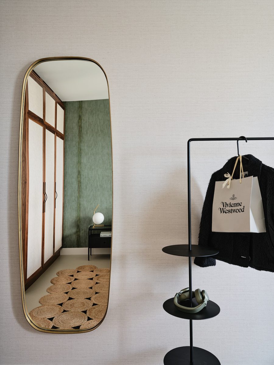 ovale spiegel tegen beige behang en zwart stalen kledingrek
