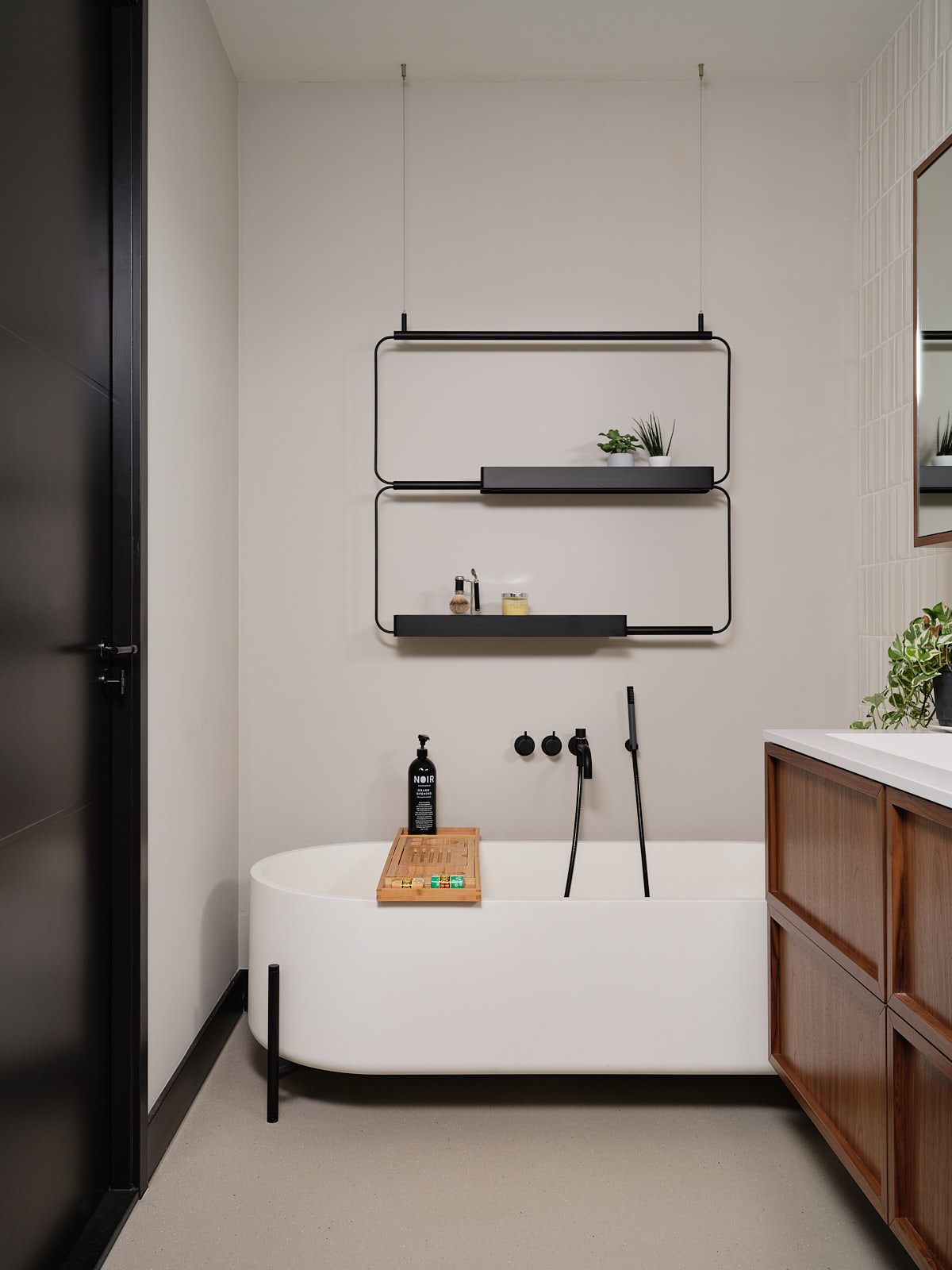 moderne badkamer met vrijstaand bad op pootjes, zwart stalen wandrek, zwarte deuren en plinten, notenhouten wastafel en witte tegeltjes