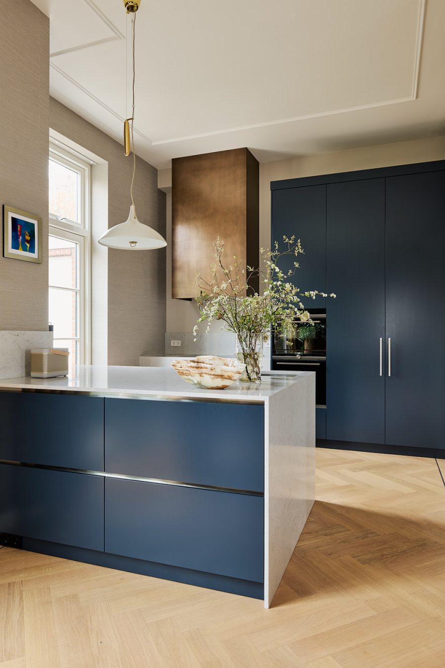 keuken met blauwe kasten en kookeiland, bronzen afzuigkap en een wit marmeren aanrechtblad