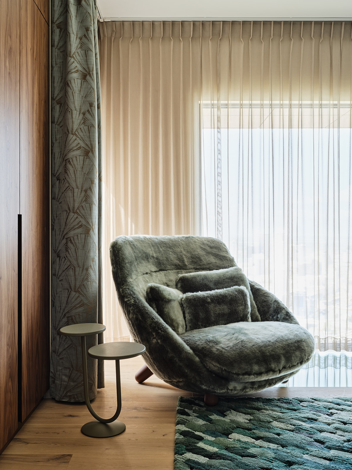 slaapkamer met een fauteuil gestoffeerd met groen nepbont, noten houten hoge kasten, blauw hoogpolig vloerkleed, gouden vitrages en blauwe gordijnen