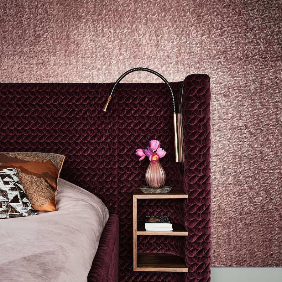 slaapkamer met een paars gestoffeerd met, paars glanzend behang op de wanden en nachtkastje en leeslampje gemonteerd aan het bed