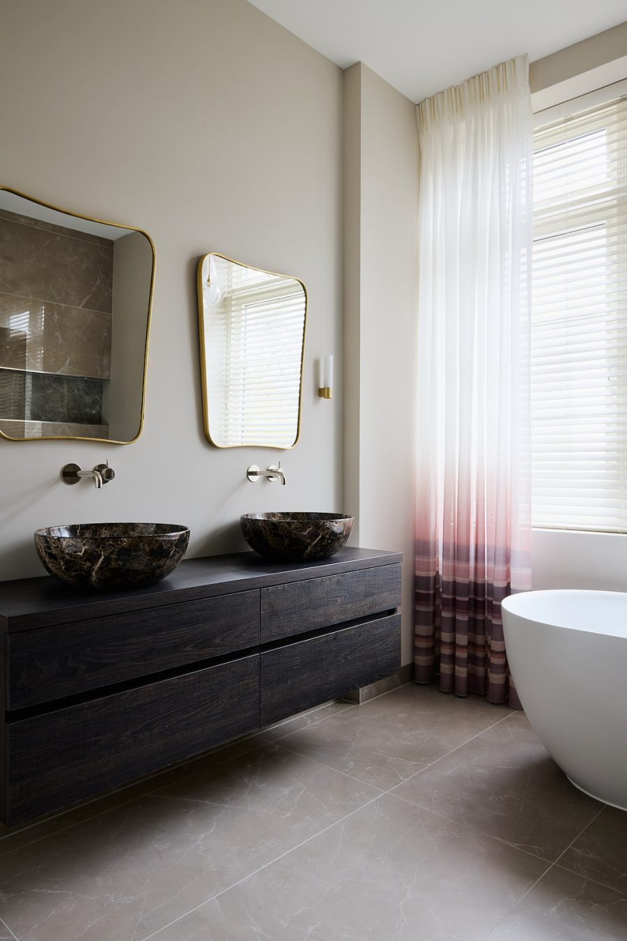 badkamer met marmeren vloer, maatwerk wastafel van donker bruin hout, marmeren ronde waskommen, gouden spiegels en degrade gordijnen