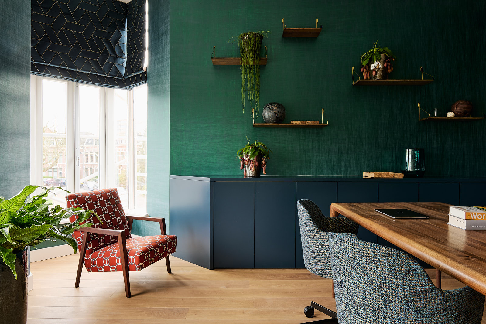 thuis kantoor met fel groen behang, lage donkerblauwe kasten, rode hermes stof, donkerblauwe bureaustoelen en donkerblauwe vouwgordijnen.