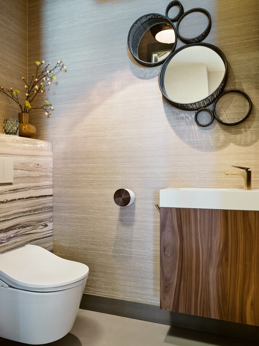 toilet met beige behang, grijs marmeren planchet, noten houten wastafel en meerdere ronde rieten spiegels in verschillende maten