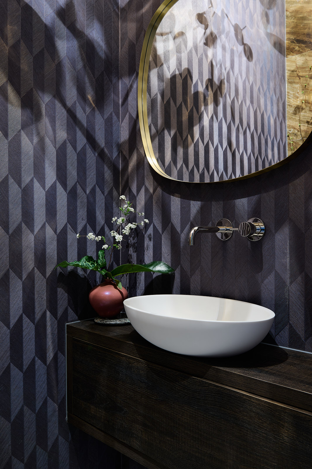 toilet met paars geometrisch behang, donker houten wastafel met witte ronde waskom en gouden ronde spiegel