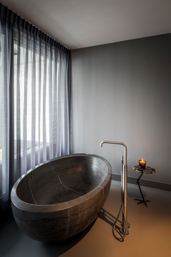 badkamer met vrijstaande massief natuurstenen bad met chroom staande kraan en paarse vitrage.