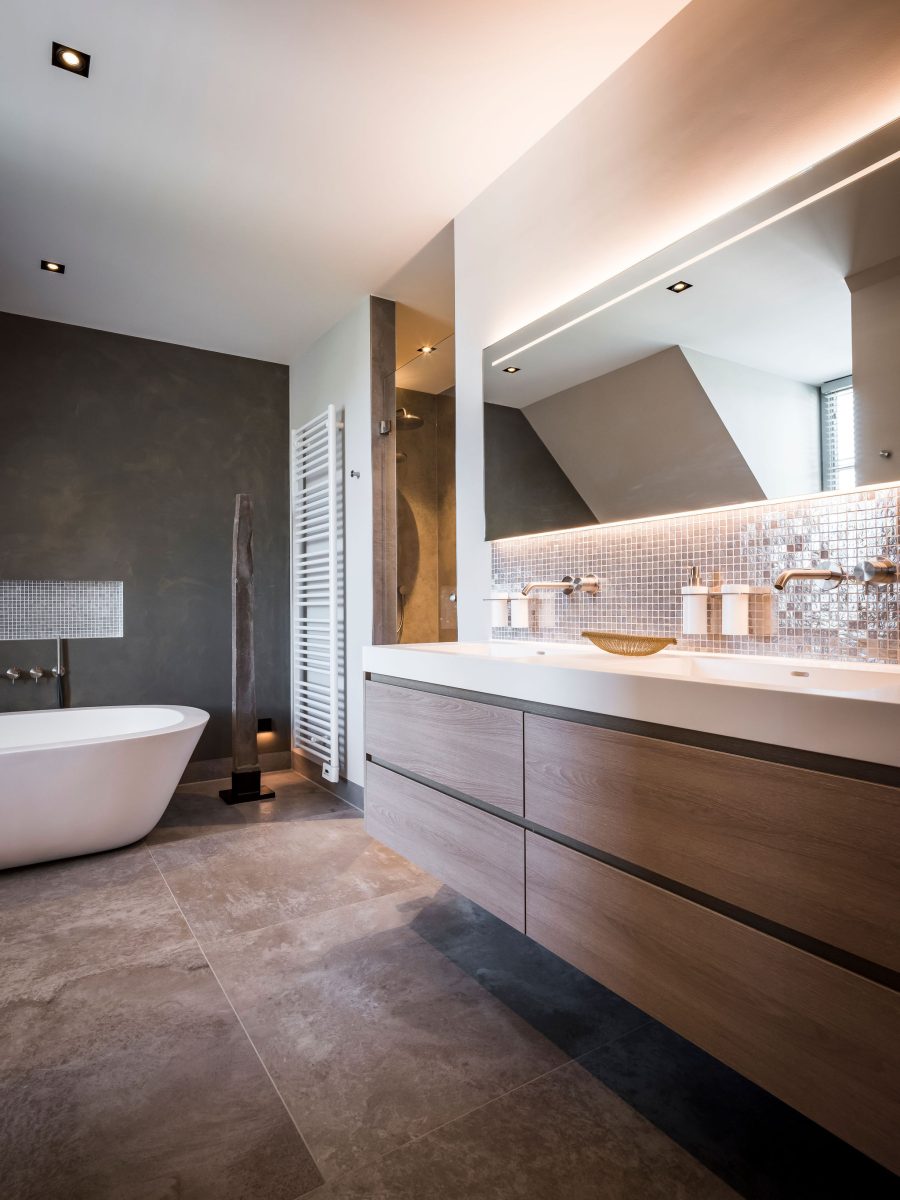 moderne badkamer met licht houten wastafel, spiegel met verlichting, roze tegeltjes, natuursteen vloer en vrijstaand wit bad