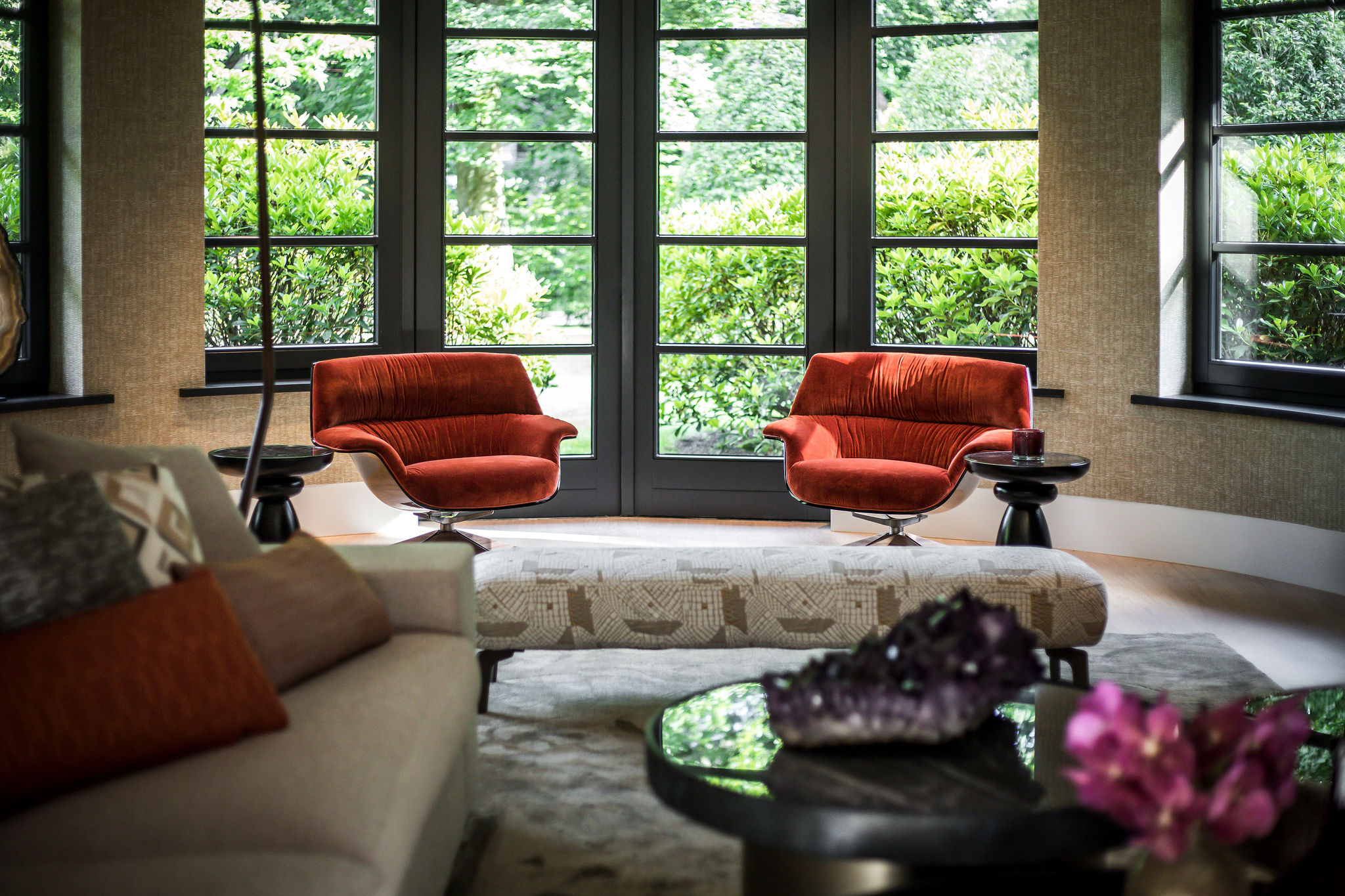 zithoekje met oranje fauteuils met zwarte bijzettafels bij grote ramen