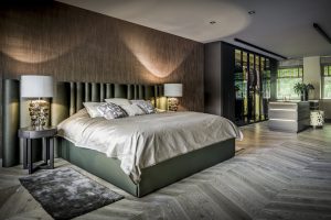 luxe slaapkamer suite met groen satijnen, visgraat vloer, bruin glanzend behang en ronde donker houten nachtkastjes met glazen aparte tafellampen.