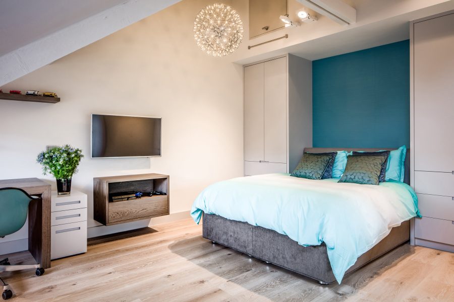 jongens kamer met grijs gestoffeerd bed, blauwe achterwand grijze maatwerke kasten en blauw beddengoed