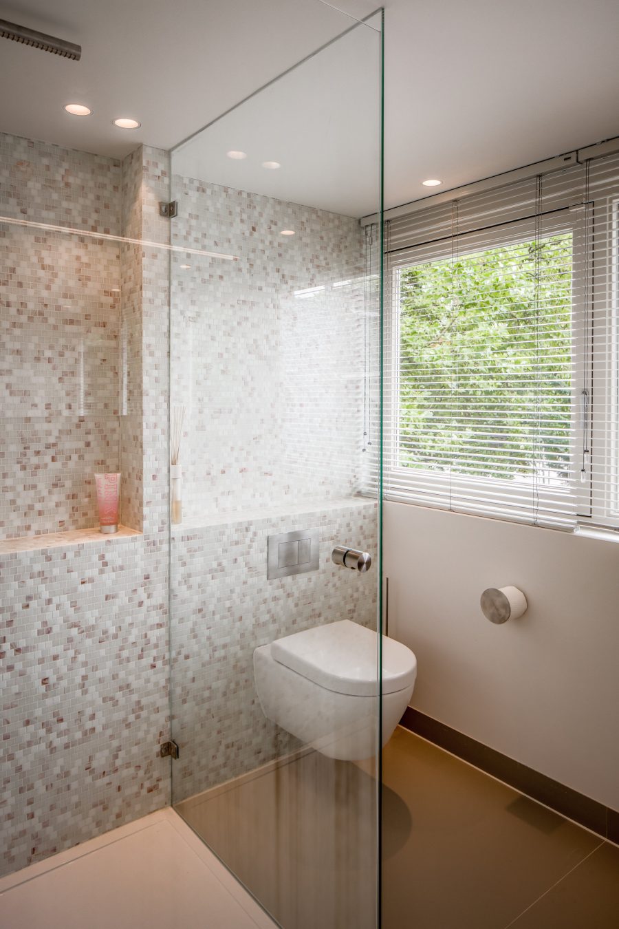 neutrale badkamer met witte roze en grijze kleine tegeltjes op de wand en champagne kleurig sanitair.