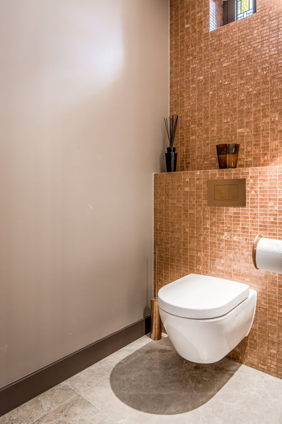 toilet met oranje tegels op de wand en planchet en een grijze natuurstenen vloer.