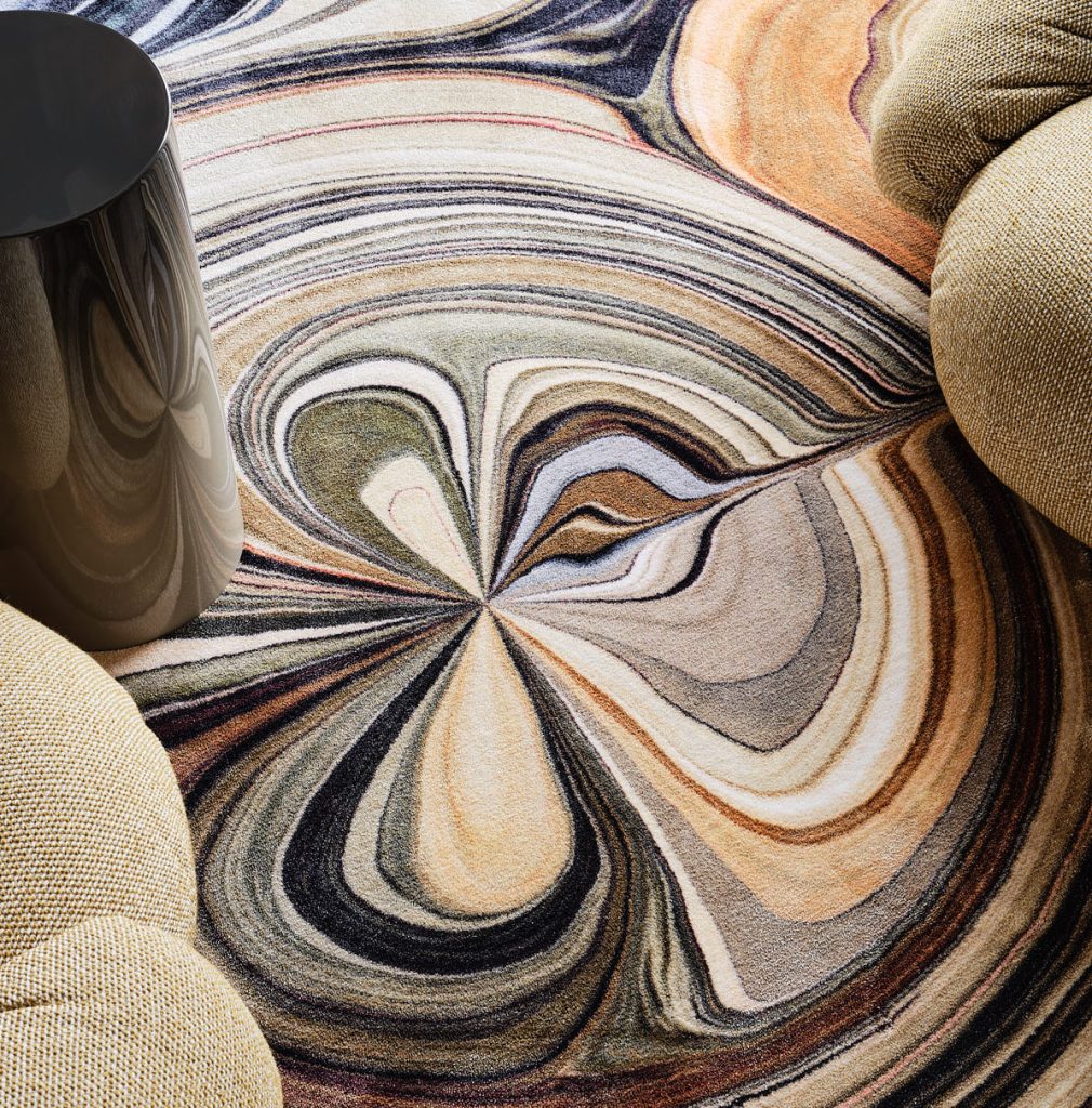 detail foto van vloerkleed met patroon dat lijkt op verf met gele gestoffeerde fauteuils en een grijze degrade bijzettafel.